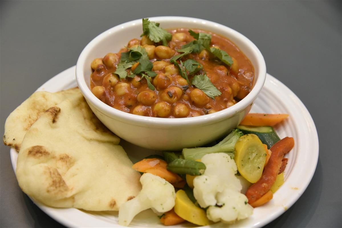 A bowl of Chana Masala, served with naan and mixed vegetables.