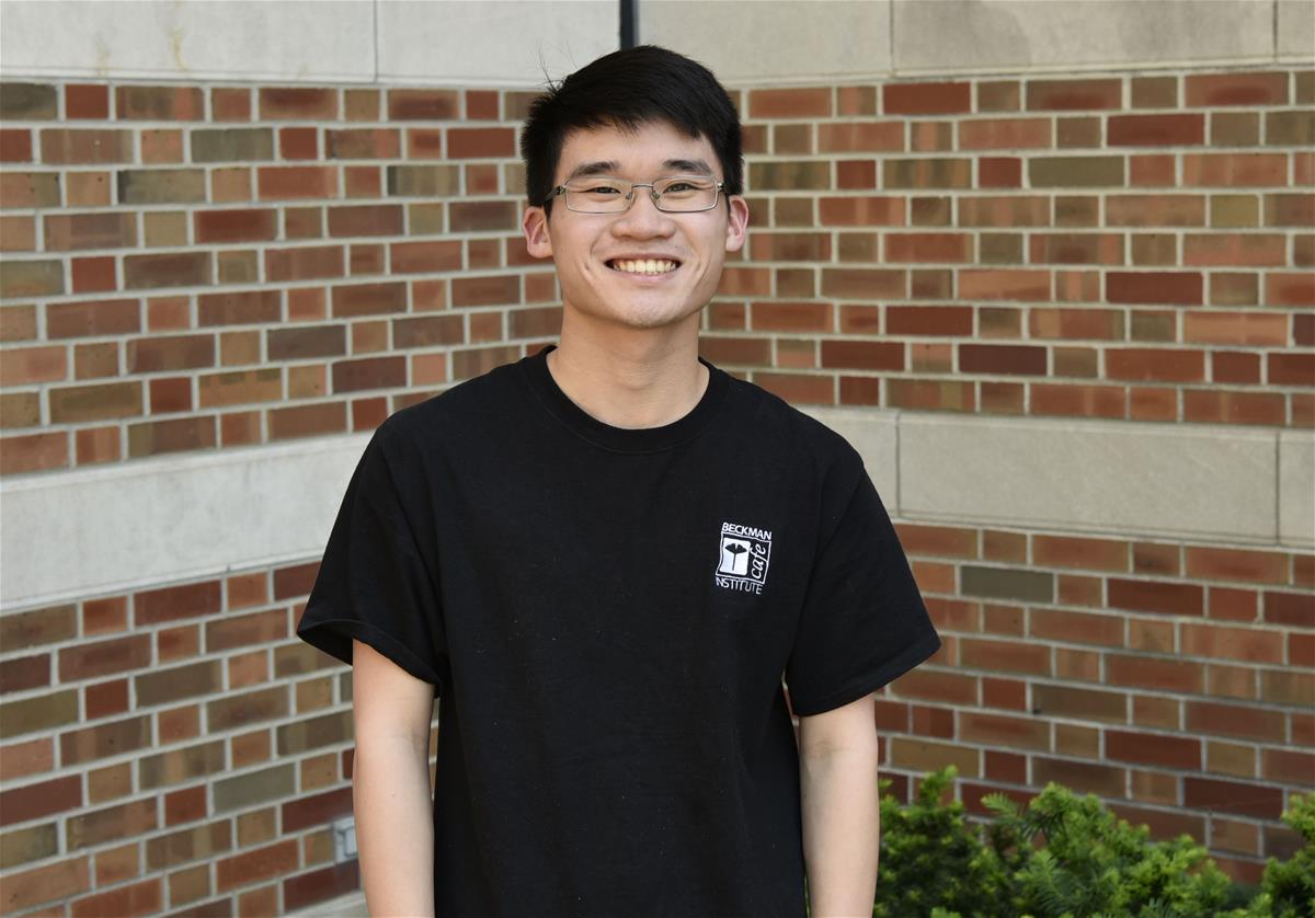 A student employee wearing a Beckman Cafe T-shirt smiles in front of an outside brick wall at the Beckman Institute at the University of Illinois at Urbana-Champaign (UIUC).