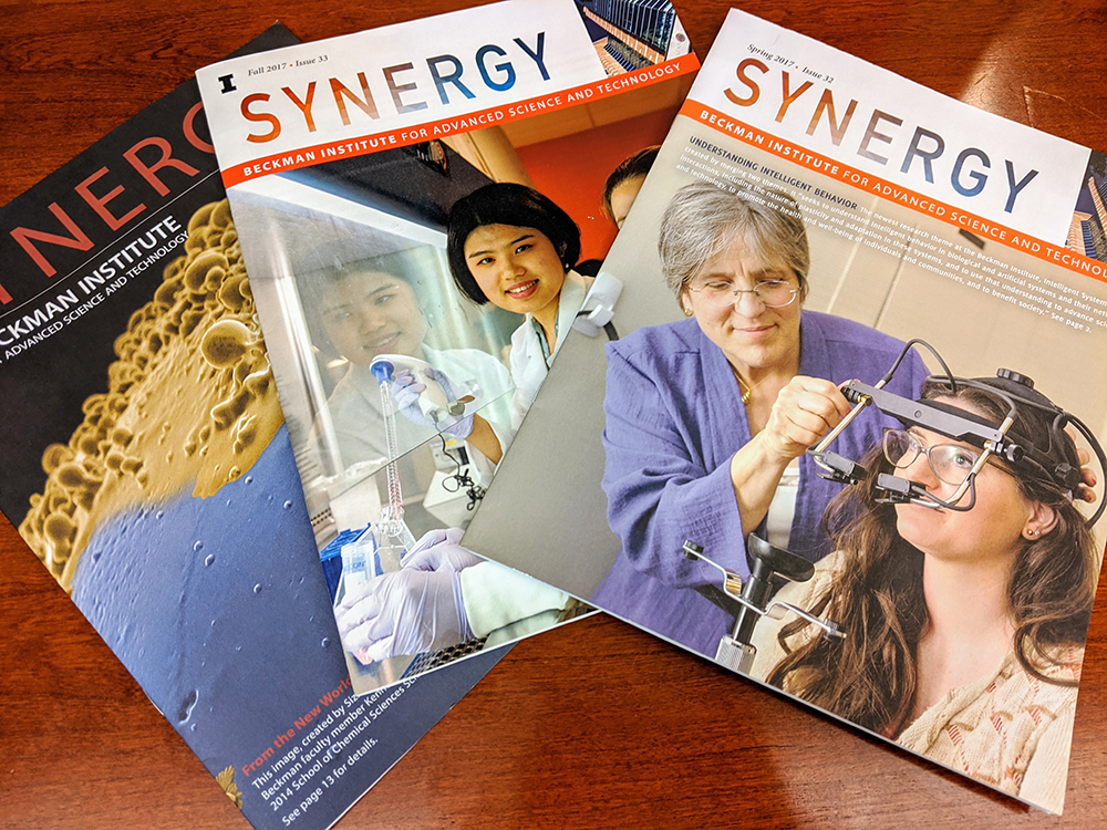 A photo of several covers of Beckman's Synergy magazine on a wood tabletop.