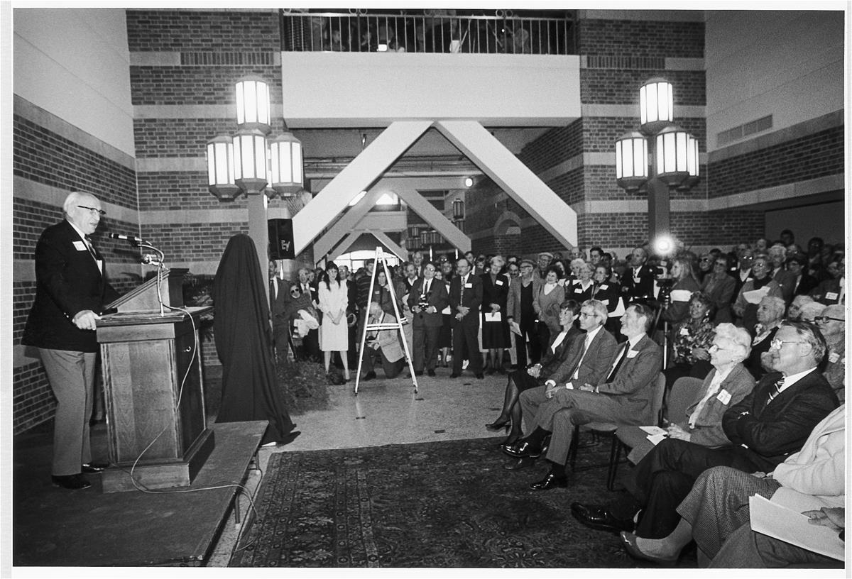 Arnold Beckman addresses a crowd in the atrium of the Beckman institute from a podium