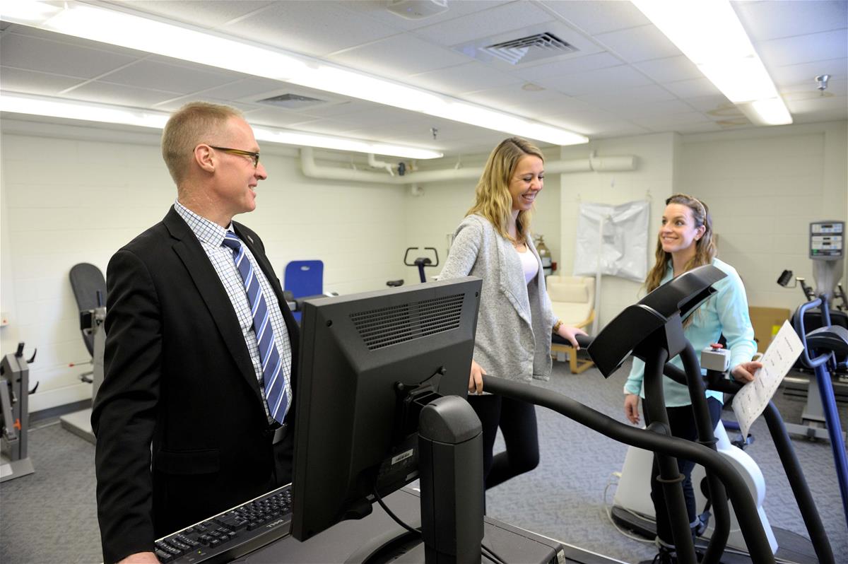 Two researchers, one behind a computer, talk to a research subject on a treadmill.