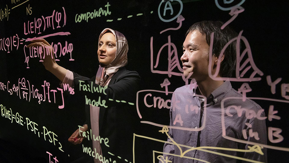 Professor Zahra Mohaghegh writes calculations on a clear wall.